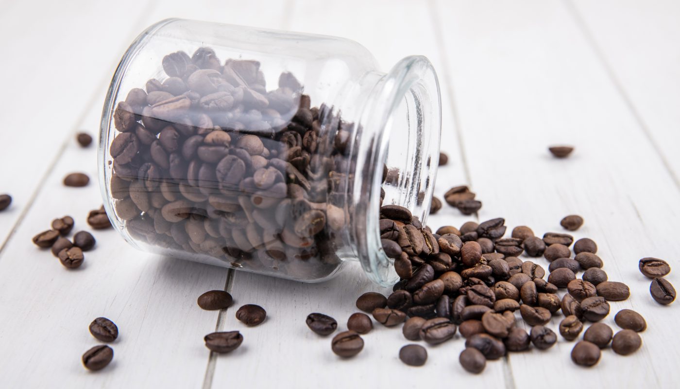 side view dark roasted coffee beans falling out glass jar white wooden background